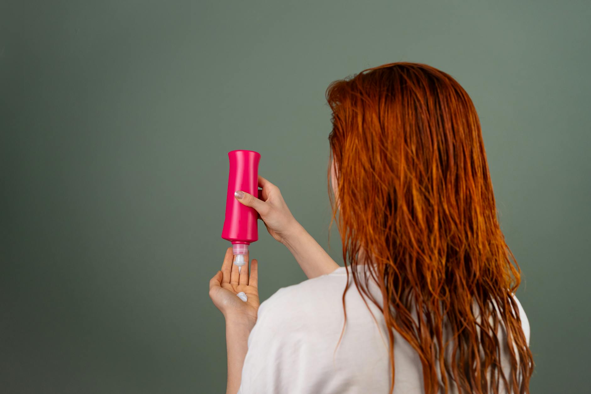 woman applying hair conditioner from red bottle